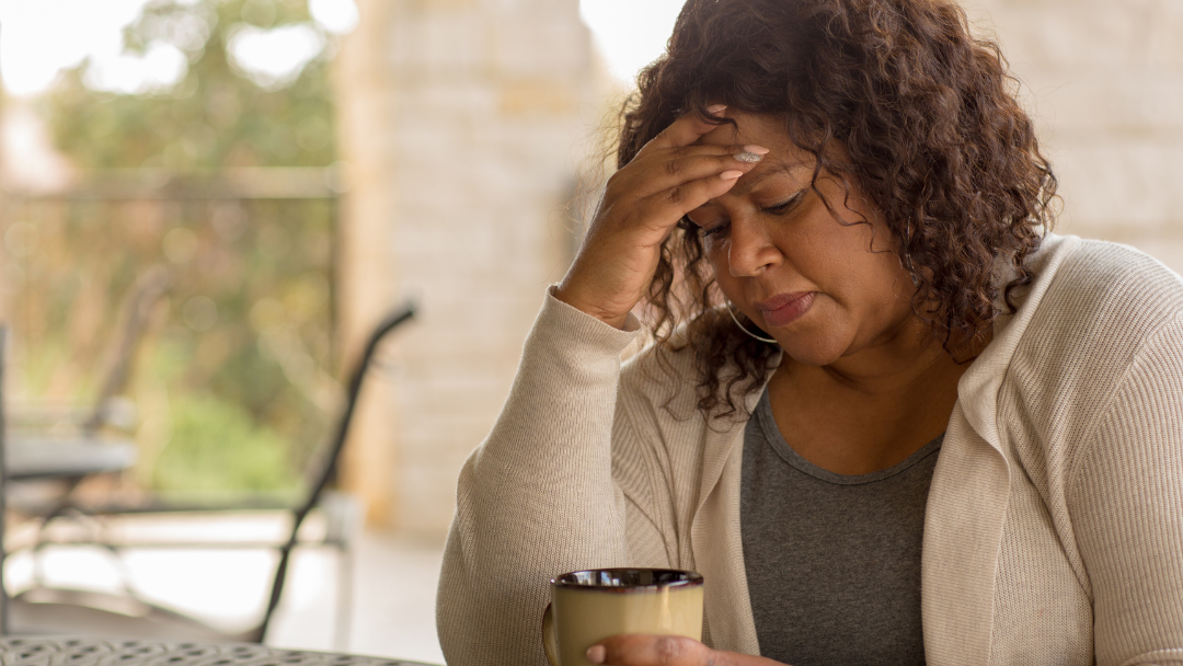 Woman sitting at table with coffee with head in hand having flashback
